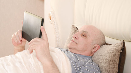 Elderly man with tablet on bed.の写真素材