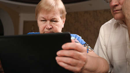 An elderly couple use modern gadgets to surf the Internet.の写真素材