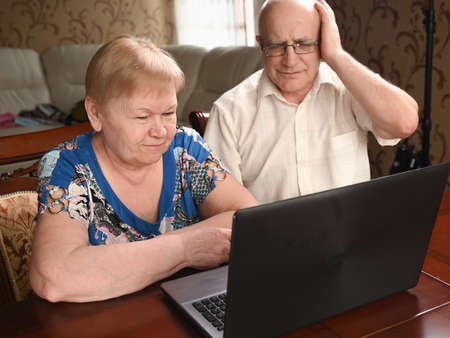 Elderly married couple sitting at the computer upset by what they saw.の写真素材