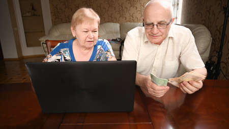 Elderly married couple sitting at the computer makes purchases on the Internet.の写真素材