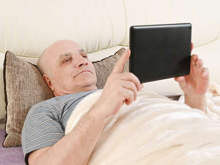 Elderly man with tablet on bed.の写真素材
