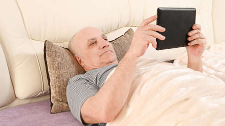 Elderly man with tablet on bed.の写真素材