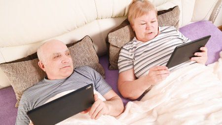 elderly couple with mobile devices in bed, top view.の写真素材