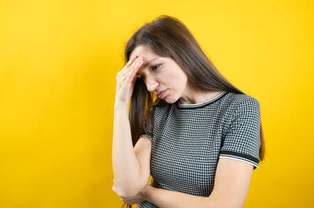 Portrait of a headache in a young girl, on a yellow background.の写真素材
