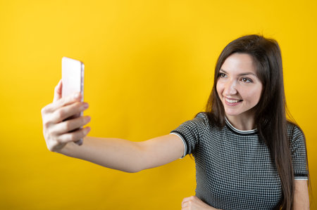A young girl communicates through a cell phone camera, on a yellow background