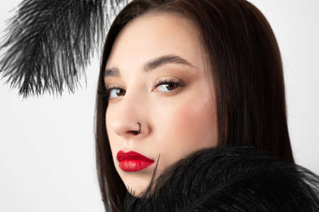 Creative stylish portrait of caucasian model girl with red lips and black feathers around her head, side view. Beauty concept.の写真素材