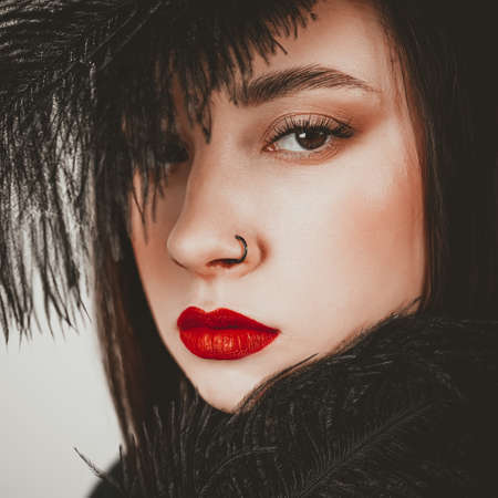 Creative stylish portrait of caucasian model girl with red lips and black feathers around her head, side view. Beauty concept.の写真素材