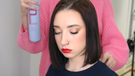 Hair master sprays varnish, makes styling. Attractive brunette in beauty salon.の写真素材