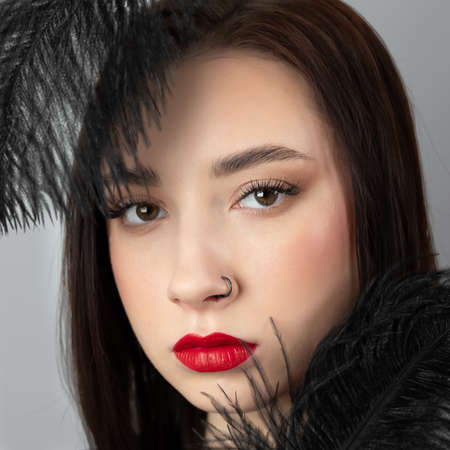 Creative stylish portrait of caucasian model girl with red lips and black feathers around her head, side view. Beauty concept.の写真素材