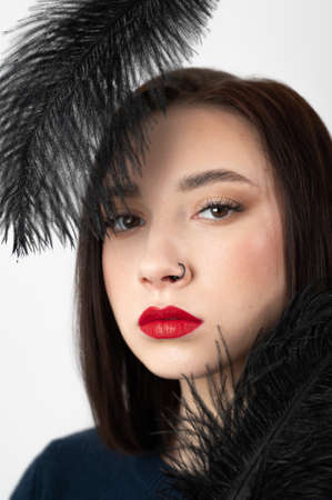 Creative stylish portrait of caucasian model girl with red lips and black feathers around her head, side view. Beauty concept.の写真素材