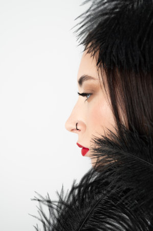 Creative stylish portrait of caucasian model girl with red lips and black feathers around her head, side view. Beauty concept.の写真素材