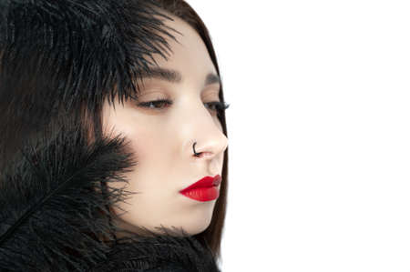 Creative stylish portrait of caucasian model girl with red lips and black feathers around her head, side view. Beauty concept.の写真素材