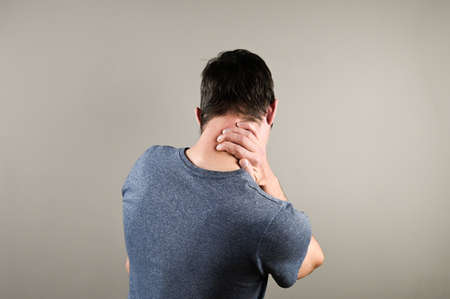 Man massaging his neck on gray background. Suffering from discomfort long hours of sedentary overworking concept. High quality photoの写真素材