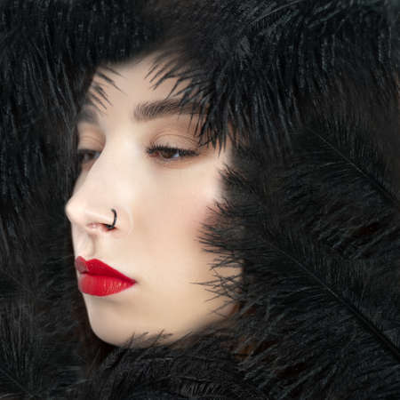 Creative stylish portrait of caucasian model girl with red lips and black feathers around her head. Beauty concept.の写真素材