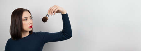 Makeup Concept. Young brunette holding cosmetic brush over beige background, bannerの写真素材