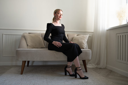 Elegant woman in black dress sits on the sofa.