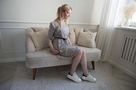 Portrait of a beautiful blonde in a dress sitting on the sofa.の写真素材