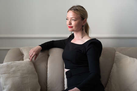 Elegant woman in black dress sits on the sofa.の写真素材