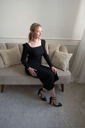 Elegant woman in black dress sits on the sofa.の写真素材