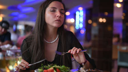 Vegetarian woman enjoying vegetable salad, evening in restaurant.の写真素材