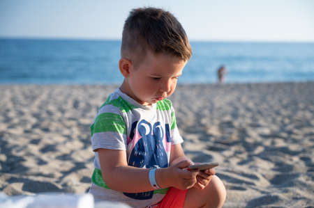 Child holding a stone while sitting on the beachの写真素材