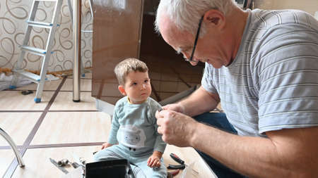 Grandfather plays with his grandson, show tools at homeの写真素材