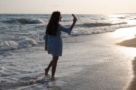 Young woman taking pictures of herself against the background of the sea.の写真素材