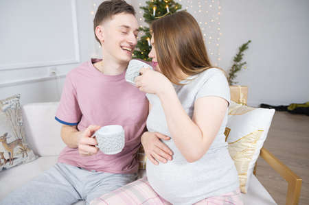 Happy couple drinking tea or coffee at home in evening over christmas tree lights on background. Holidays, leisure and people concept.の写真素材