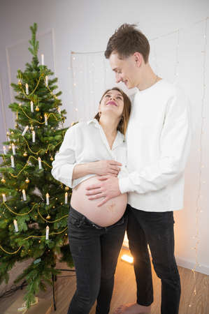 Pregnant woman with naked belly hugs her husband. Waiting for Christmas and babyの写真素材