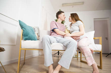 Portrait of smiling young couple sitting on sofa at home and spending time together while dreamily looking on each other.の写真素材