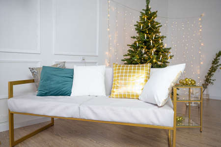 Living room with a sofa and a large Christmas tree and copy space over white wall with lights. New Year's interior.の写真素材