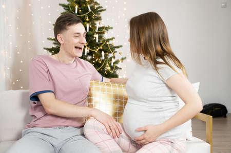 Happy charming couple at home for Christmas. Happy husband and pregnant wife laughing, holidays conceptの写真素材