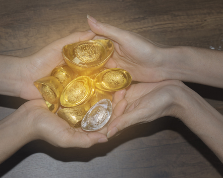 Decoration of chinese gold ingots in hand on wood background,Translation in English meaning lucky and richlyの写真素材