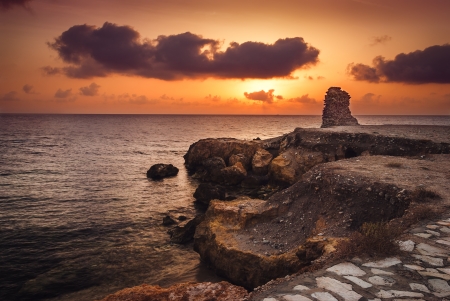 sunset over the sea and rocky coast with ancient ruinsの写真素材
