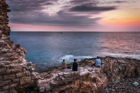 Family is Waiting for Sunset over the Sea and Rocky Coast with Ancient Ruinsの写真素材