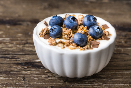 Serving of Yogurt with Whole Fresh Blueberries and Muesli on Old Rustic Wooden Table. Closeup Detail.の写真素材