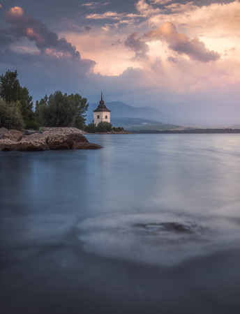 Virgin Mary Church by Liptovska Mara Lake with Western Tatras Mountains in Background at Sunset in Slovakiaの写真素材