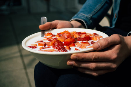 Woman holding a bowl of sliced strawberries with milk on her kneesの写真素材