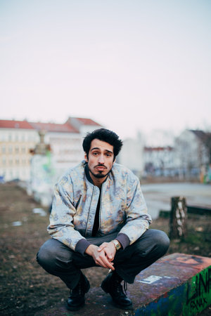 portrait of young cool arab man sitting and smoking a cigarette outdoors in urban environmentの写真素材