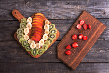 ut kiwi, banana and nectarine lying on a cutting board. Top view, old gray boards as background.の写真素材