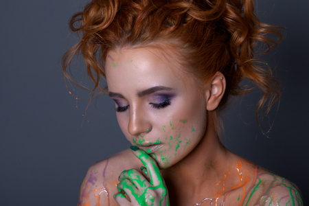 Creative portrait of a beautiful woman with red hair. With a beautiful make-up and hairdo. With paint on bodyの写真素材