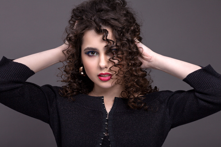 Portrait of a beautiful teenage girl with a bright make-up on a gray background. With curly hair and red lipstick.の写真素材