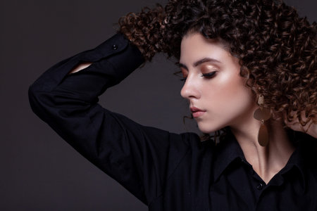 Beautiful teenager girl with afro curls and bright makeup on a dark background, black shirt.の写真素材