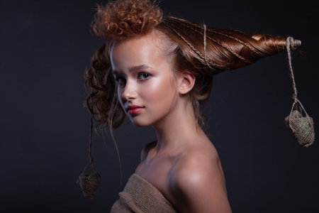 Portrait of a beautiful teenager girl with creative hairstyle and beautiful make-up on a dark background.の写真素材