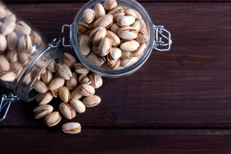 Pistachios in glass jars on a wooden background, top view.