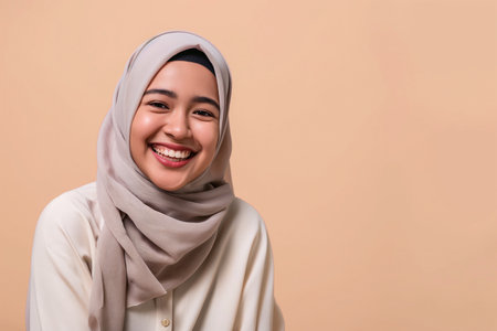 Beautiful Asian young Muslim woman wearing hijab, smiling and looking at camera on beige backgroundの素材