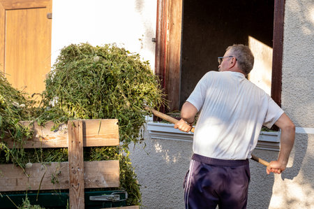 Senior man loading hay in front of his house on a sunny dayの写真素材