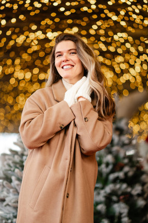 happy woman in a coat and white mittens stands in front of Christmas garlands, holiday moodの写真素材