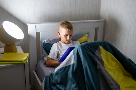 fair-haired teenage boy reading a book before bedの写真素材
