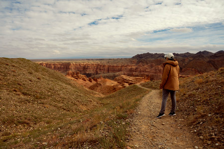 female tourist on the trail looking at the beautiful orange canyon mountains and cloudy skyの写真素材